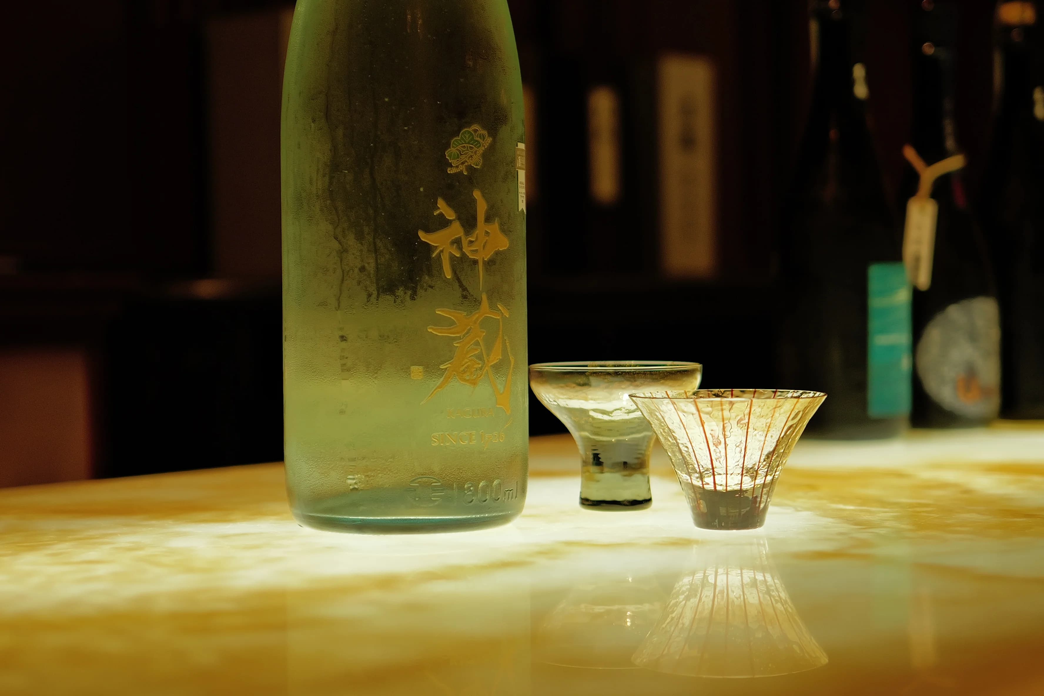 A bottle of sake and two sake glasses on a softly lit counter